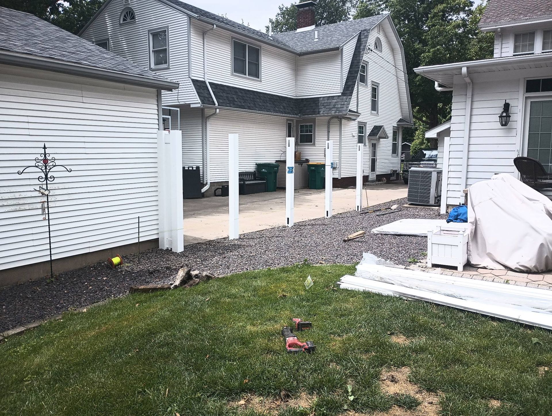 A grassy backyard featuring a gravel path and several white fence posts being installed between two white houses.