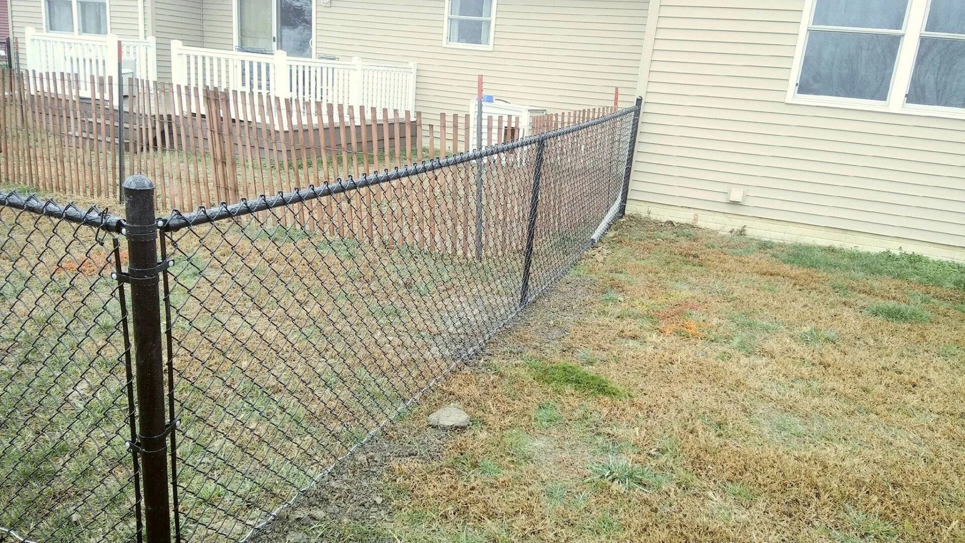 Black chain-link fence bordering a grassy area next to a beige building.
