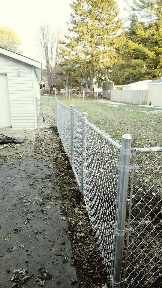 Chain-link fence running along a yard next to a garage, with some leaves on the ground.