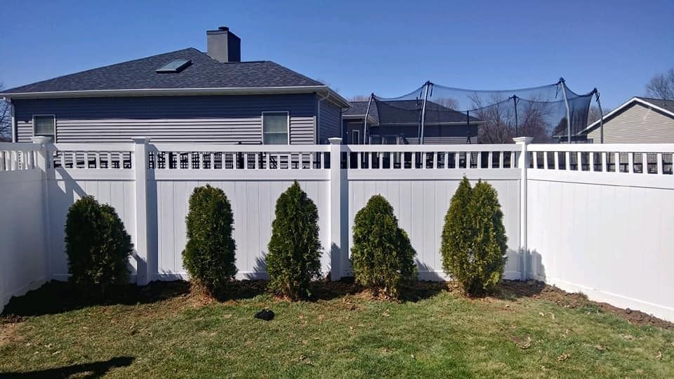 White fence with green shrubs in front of a house on a sunny day.
