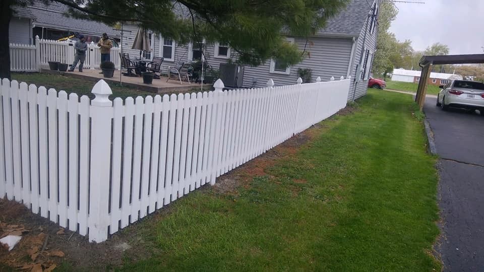 White picket fence borders a green lawn next to a driveway and a house.
