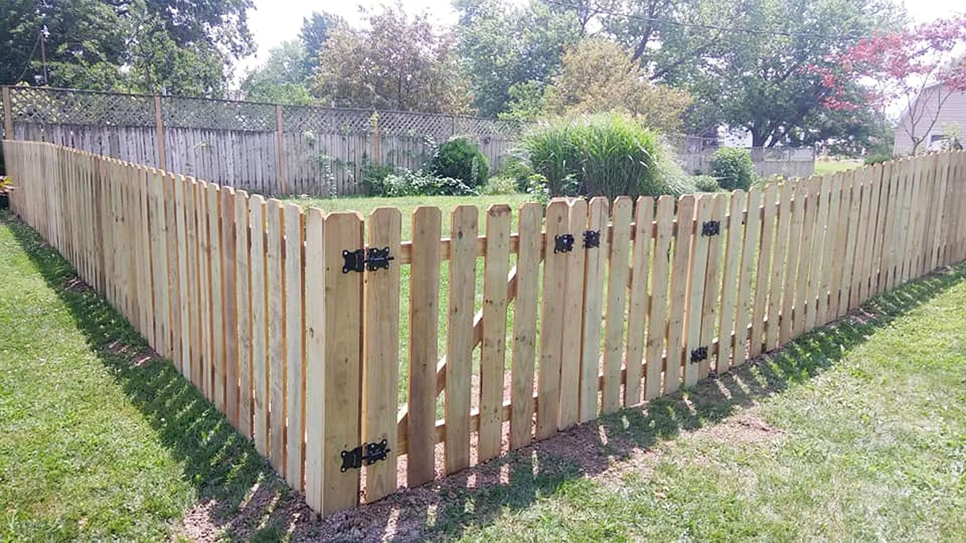 Wooden picket fence around a grassy yard with a gate, trees in the background.