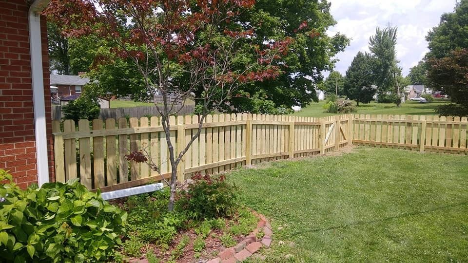 Wooden picket fence surrounding a yard with grass, a small tree, and a brick house.