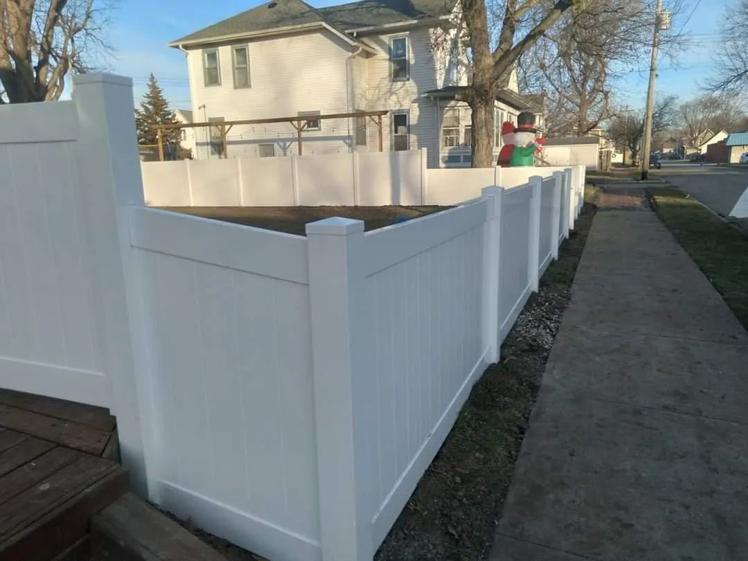 White vinyl fence surrounding a yard next to a sidewalk and house.