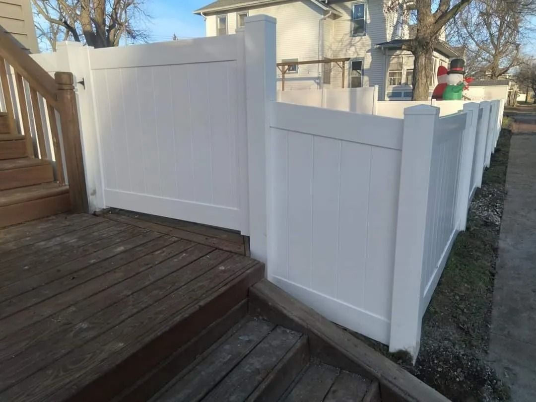 White vinyl fence next to a wooden deck. The fence runs along a yard.
