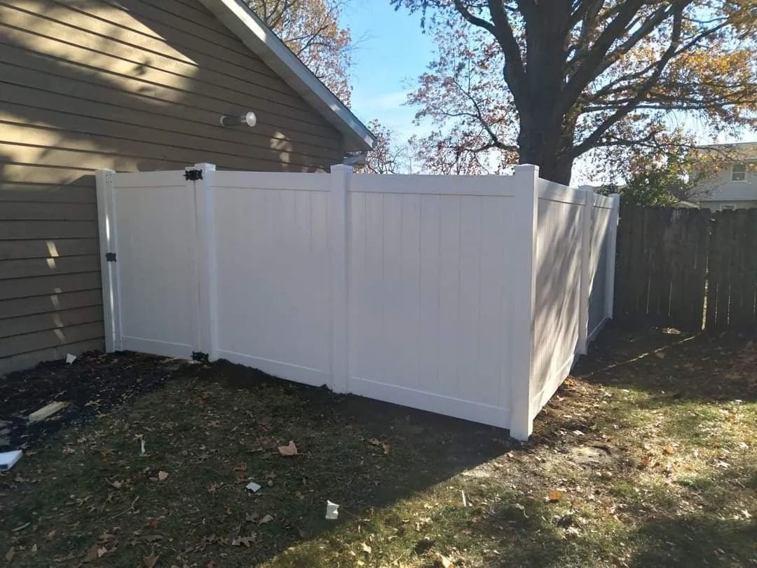 White vinyl fence cornered by a building and a tree.