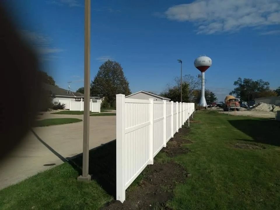 Fence posts being installed near a small building and a tree, with a wheelbarrow in the foreground.