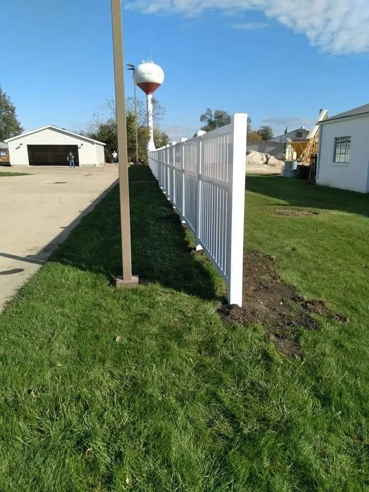 White picket fence along a grassy lawn, with a water tower visible in the distance.