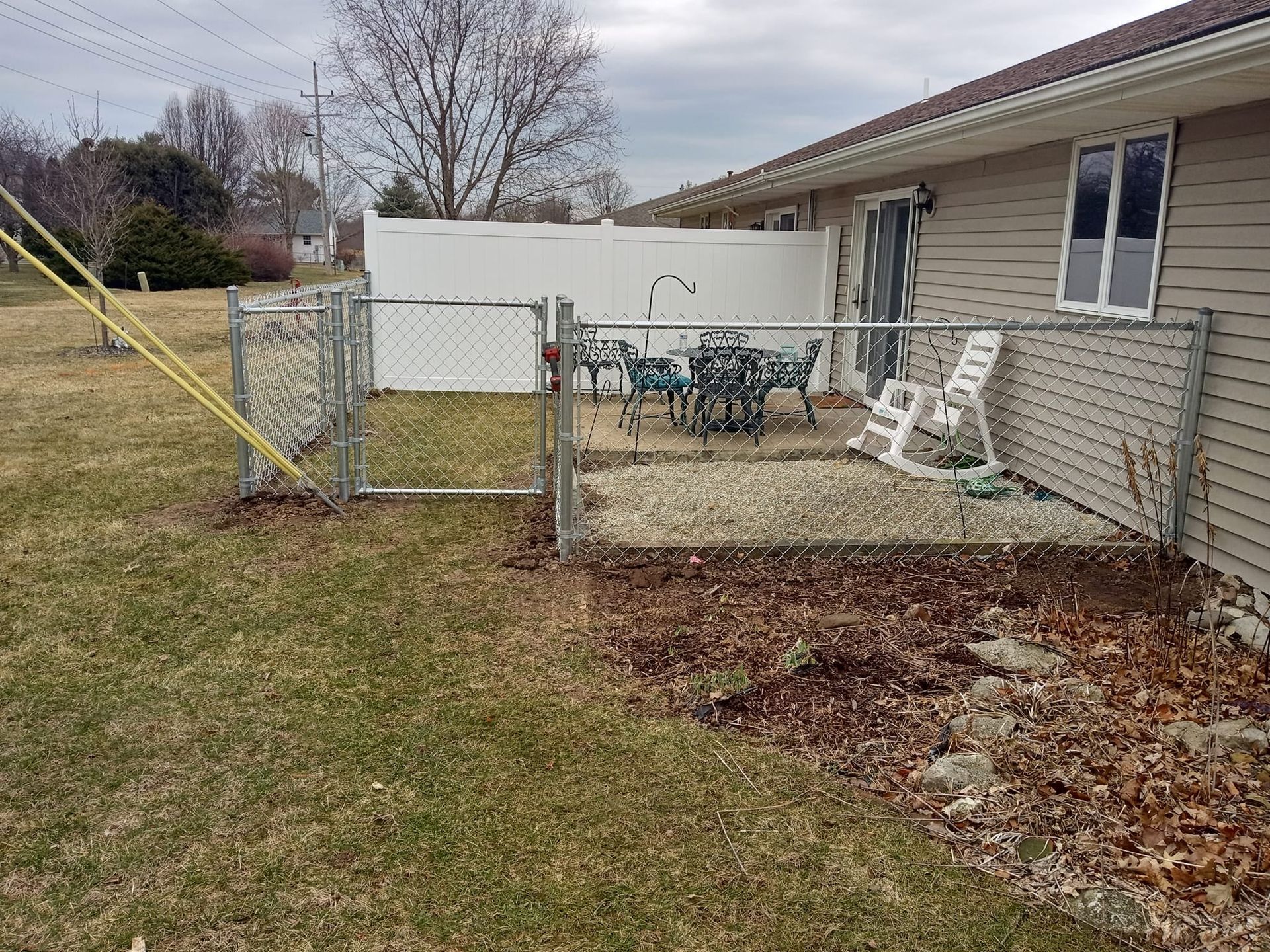 A small patio area with outdoor furniture enclosed by a chain-link fence, situated next to a house with beige siding.