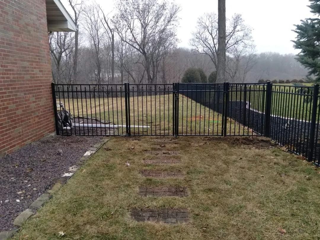 Black metal fence enclosing a grassy yard, beside a brick building.