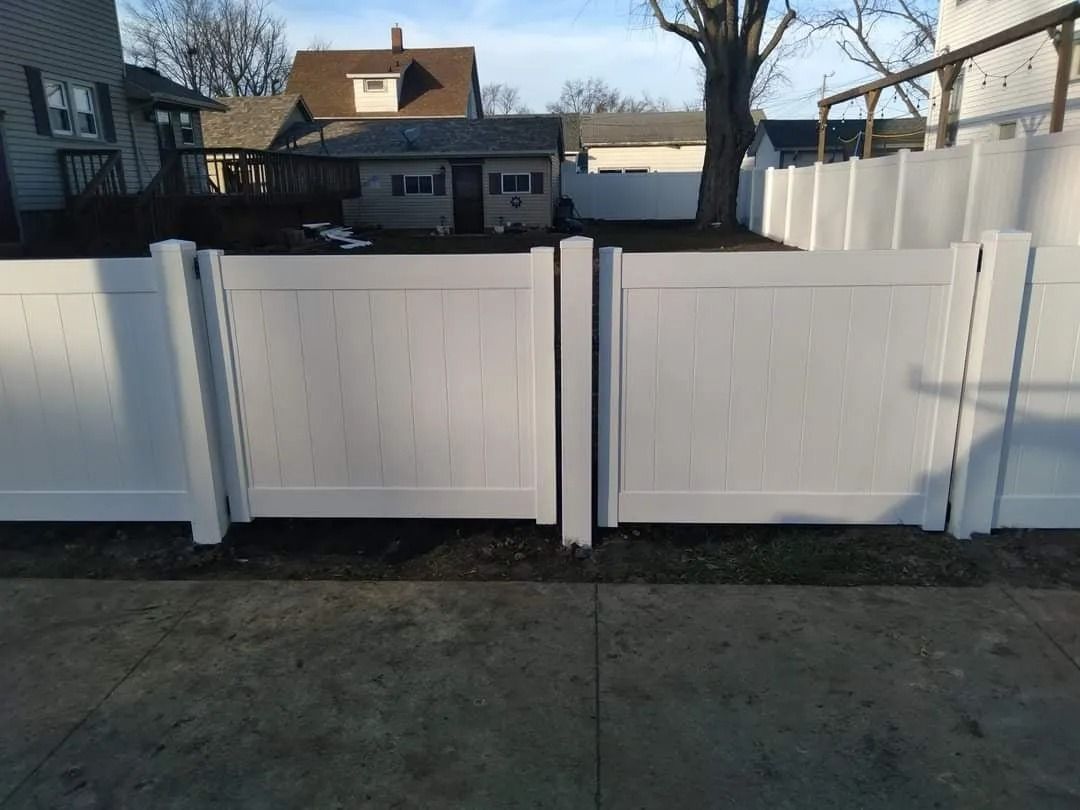 White vinyl fence with two closed gates in a residential yard.