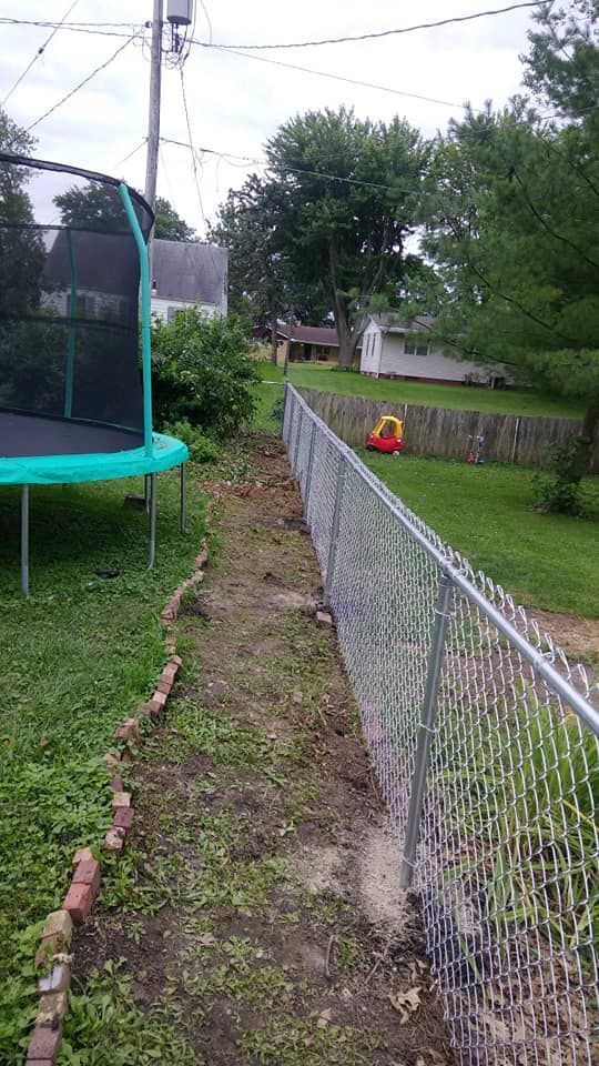 A backyard view of a trampoline next to a chain-link fence bordering a lawn with scattered bricks.