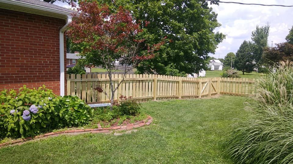 A brick house corner next to a wooden picket fence in a green, sunny residential backyard.