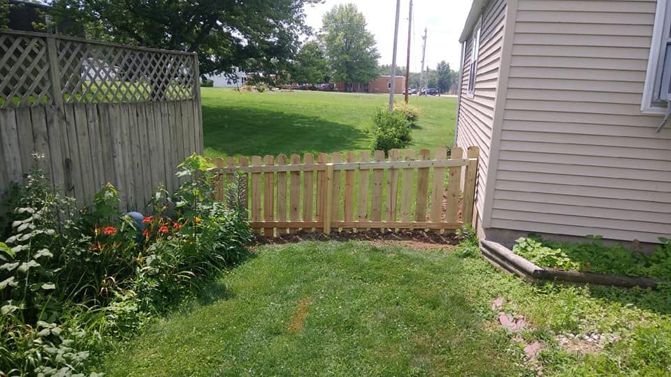 A short wooden picket fence connects a house to a taller side fence in a grassy backyard.