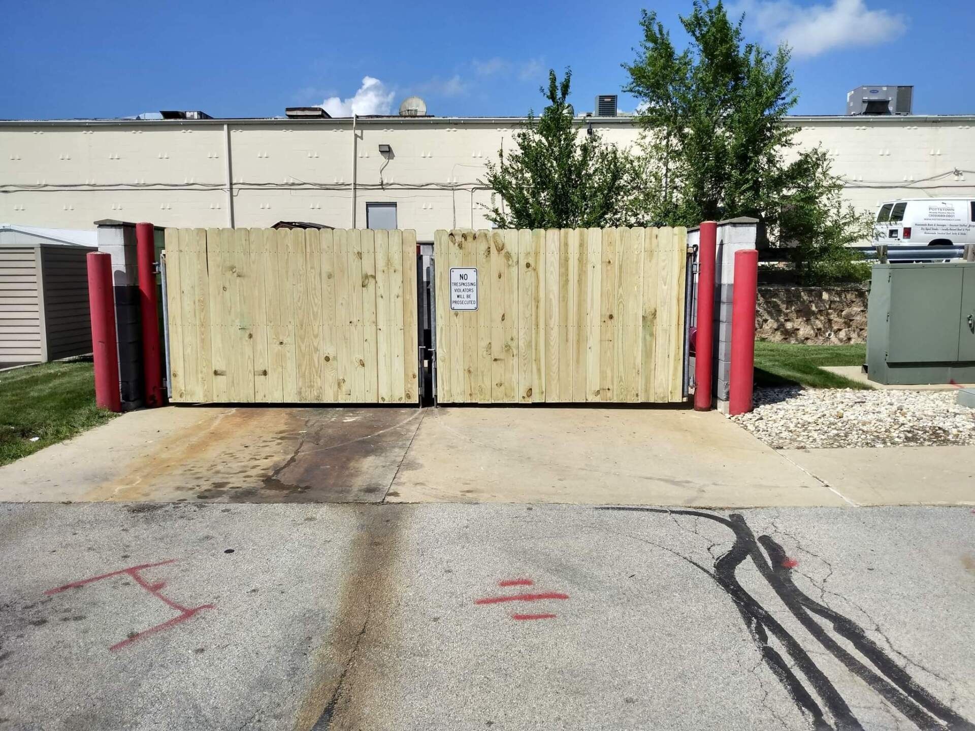 Wooden gates, with red posts, block an industrial driveway.
