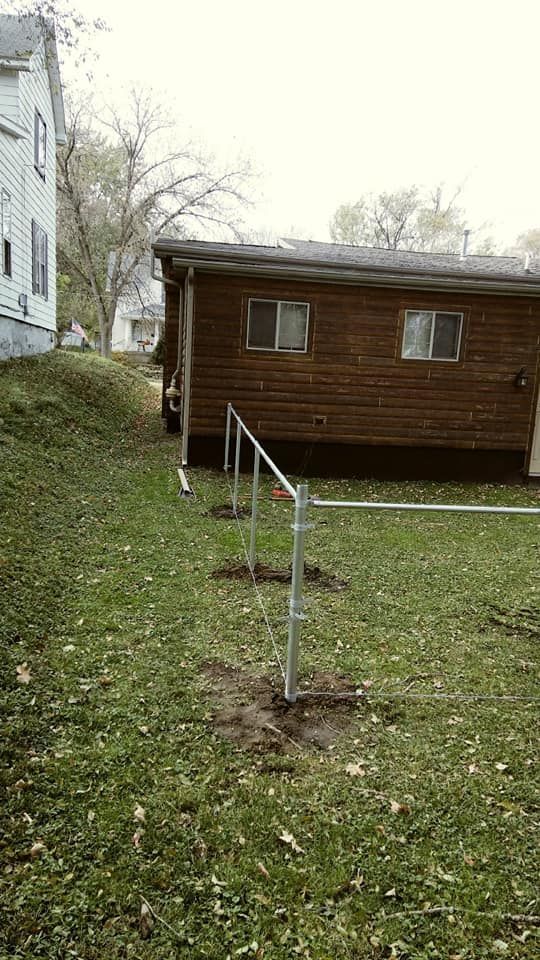 Metal fence posts installed in a grassy backyard near a brown wooden building.