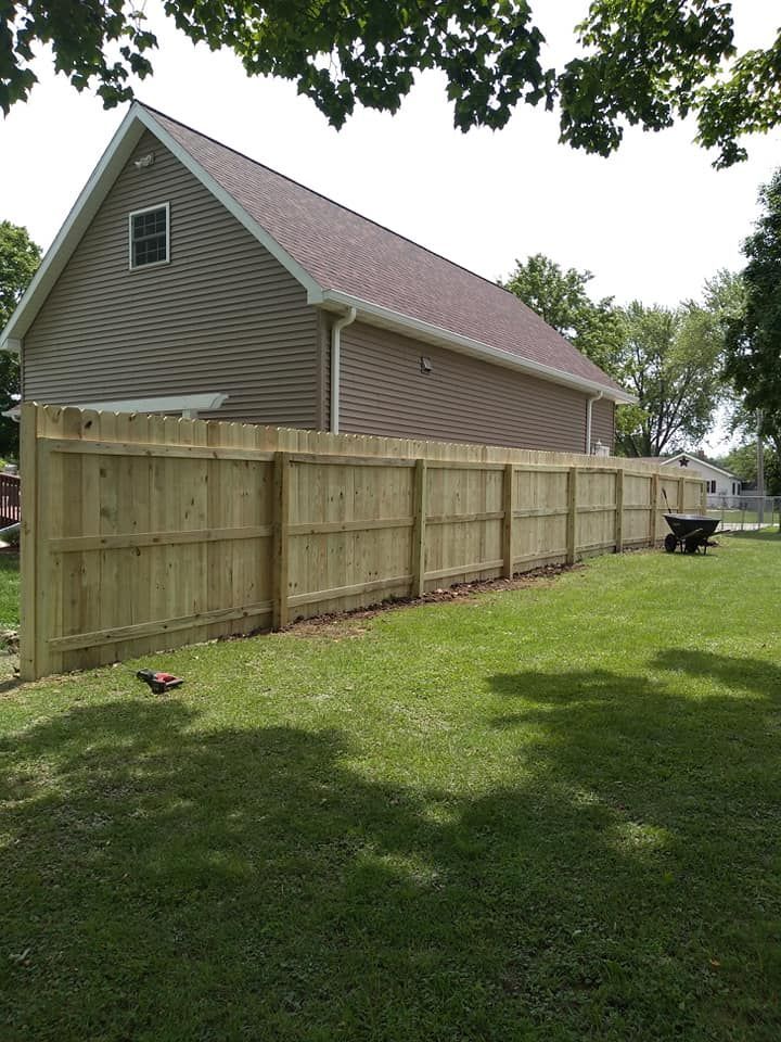 A newly installed wooden privacy fence runs alongside a tan house on a grassy lawn.