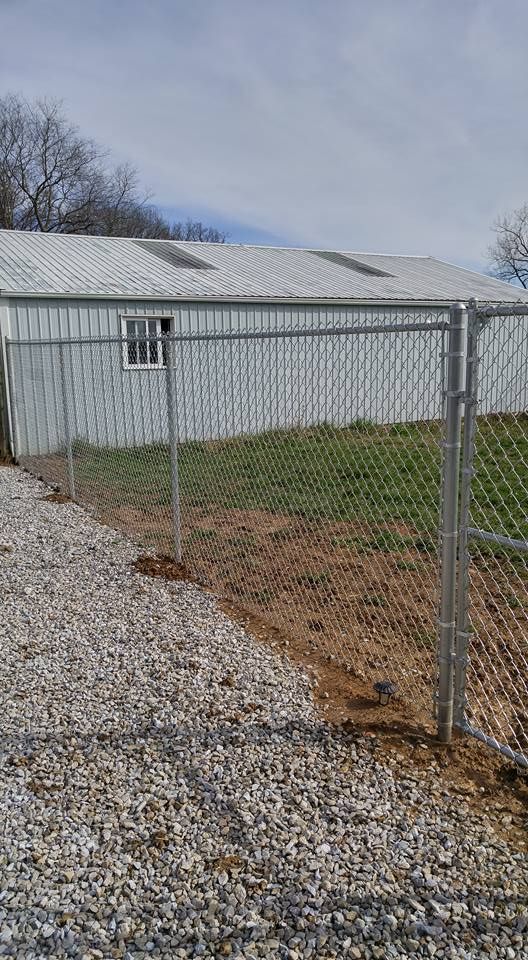 A chain-link fence stands in the foreground, with a gravel path beside it and a metal building in the background.