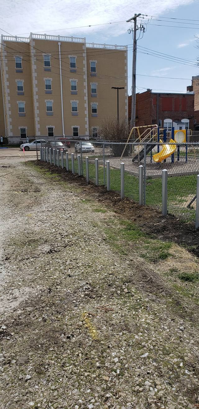 A gravel path leads to a playground with a slide and climbing structure, set against a multi-story apartment building.