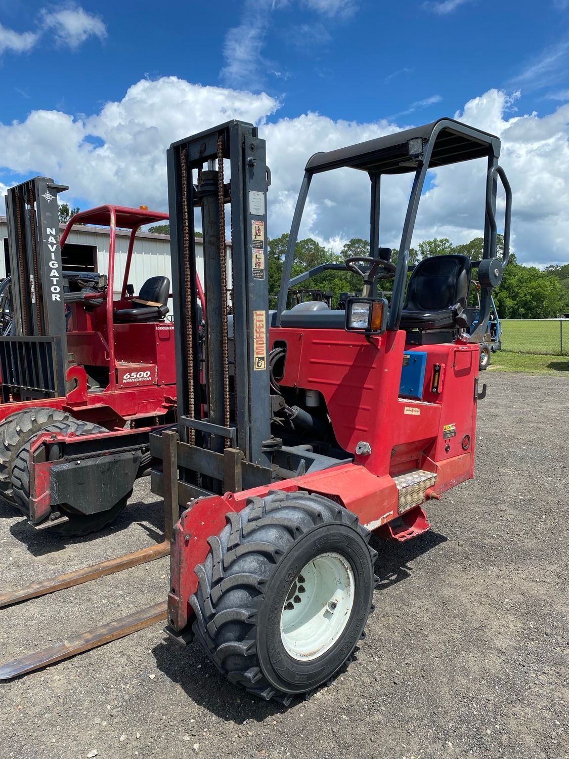 A red forklift is parked next to a black forklift in a parking lot.