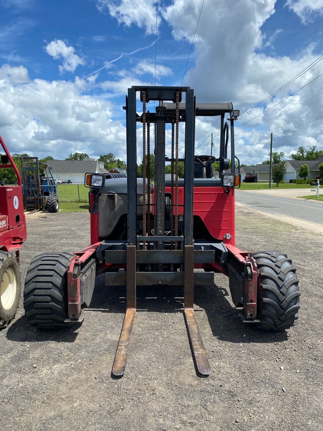 A red forklift is parked in a gravel lot.