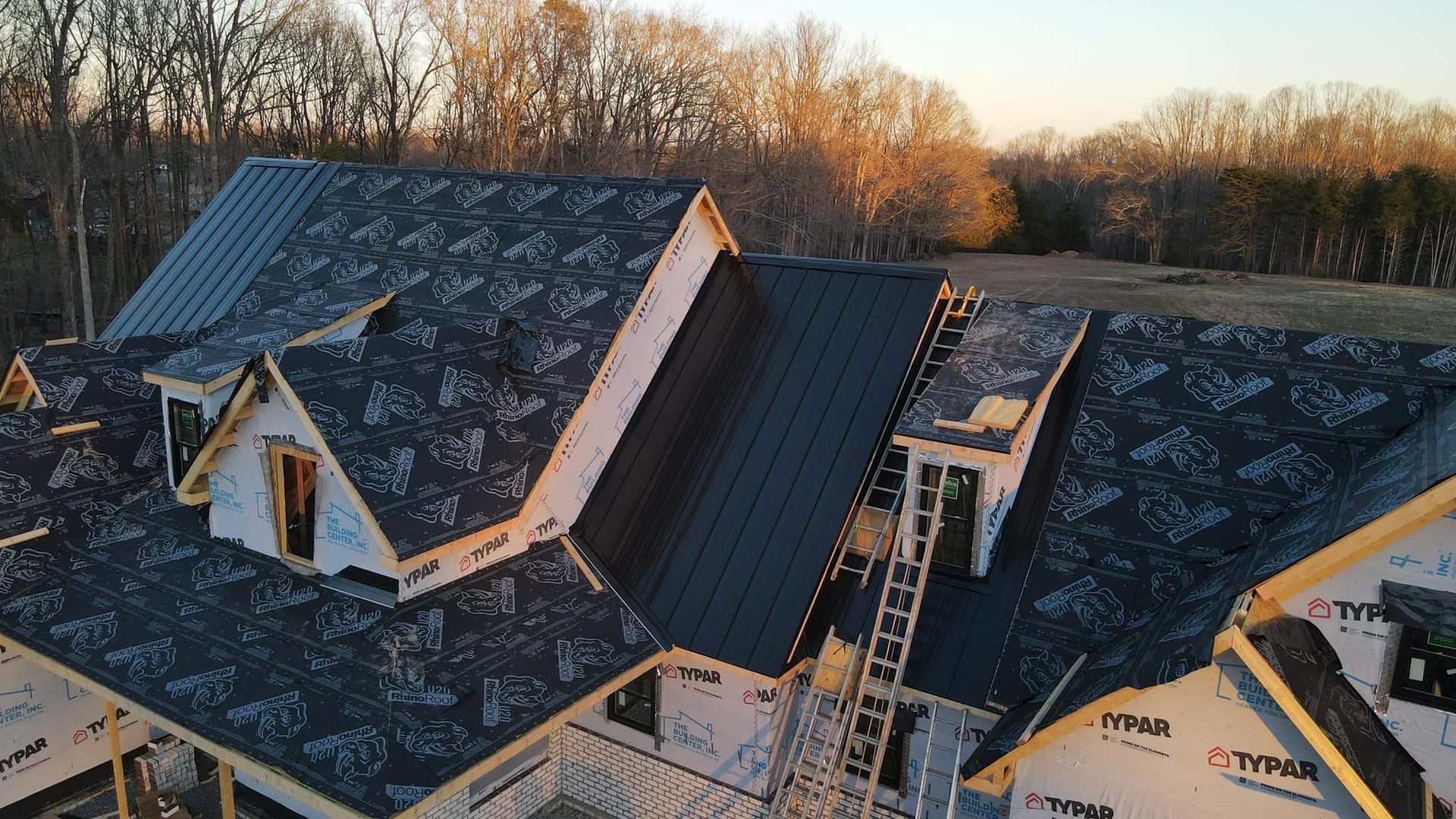 House under construction with dark metal roof; ladder on roof.