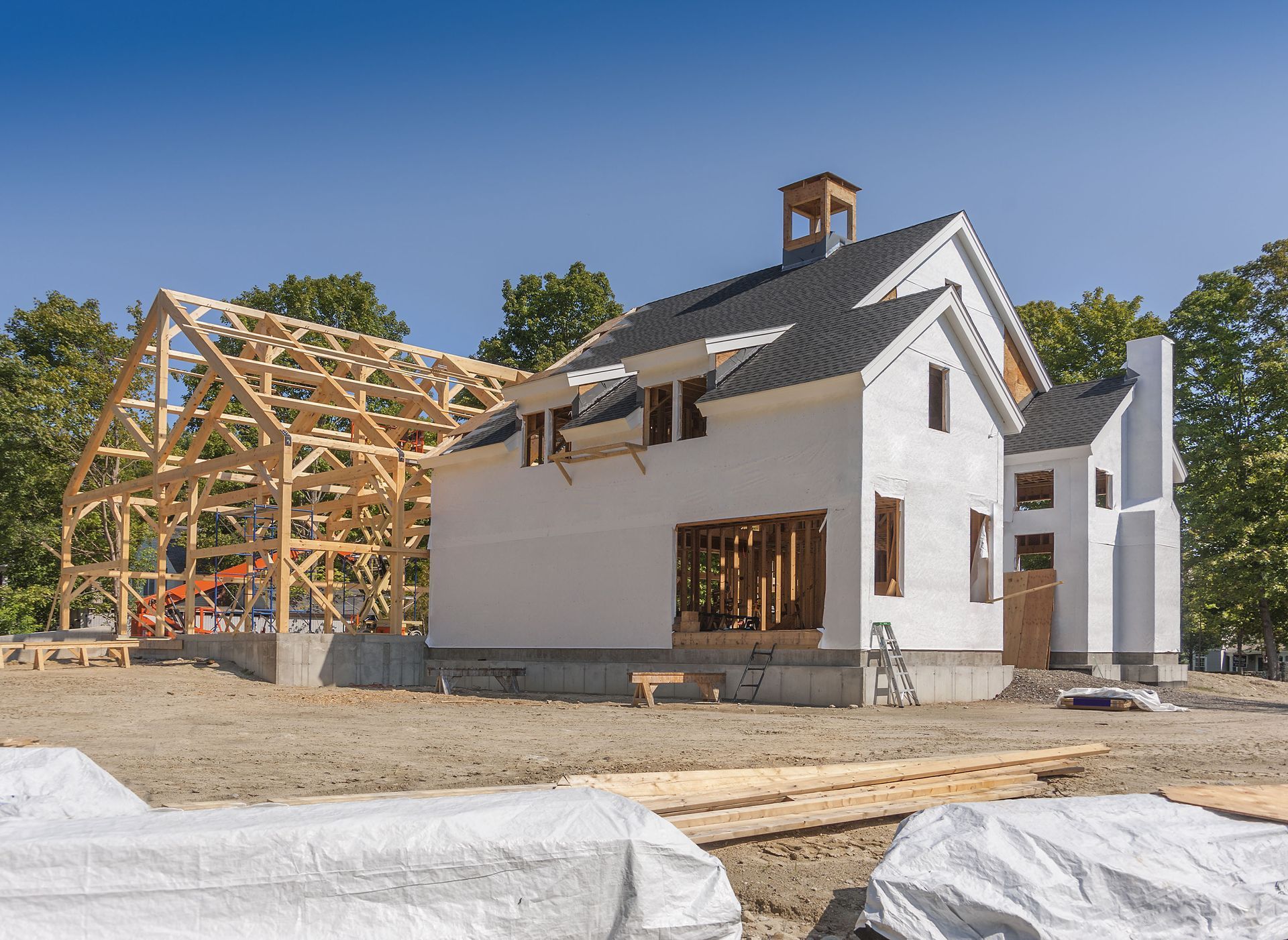 Construction site: partially built white house with exposed wooden frame and chimney, against blue sky.