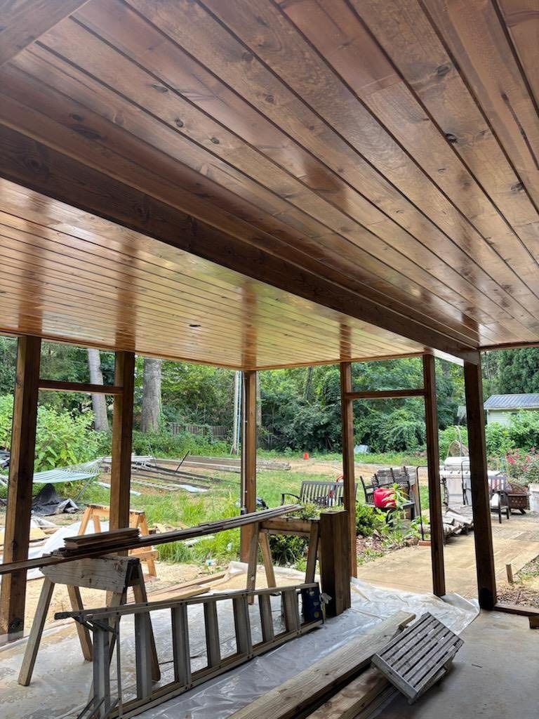 Wooden porch ceiling and supports; view overlooking a yard with tools and greenery.