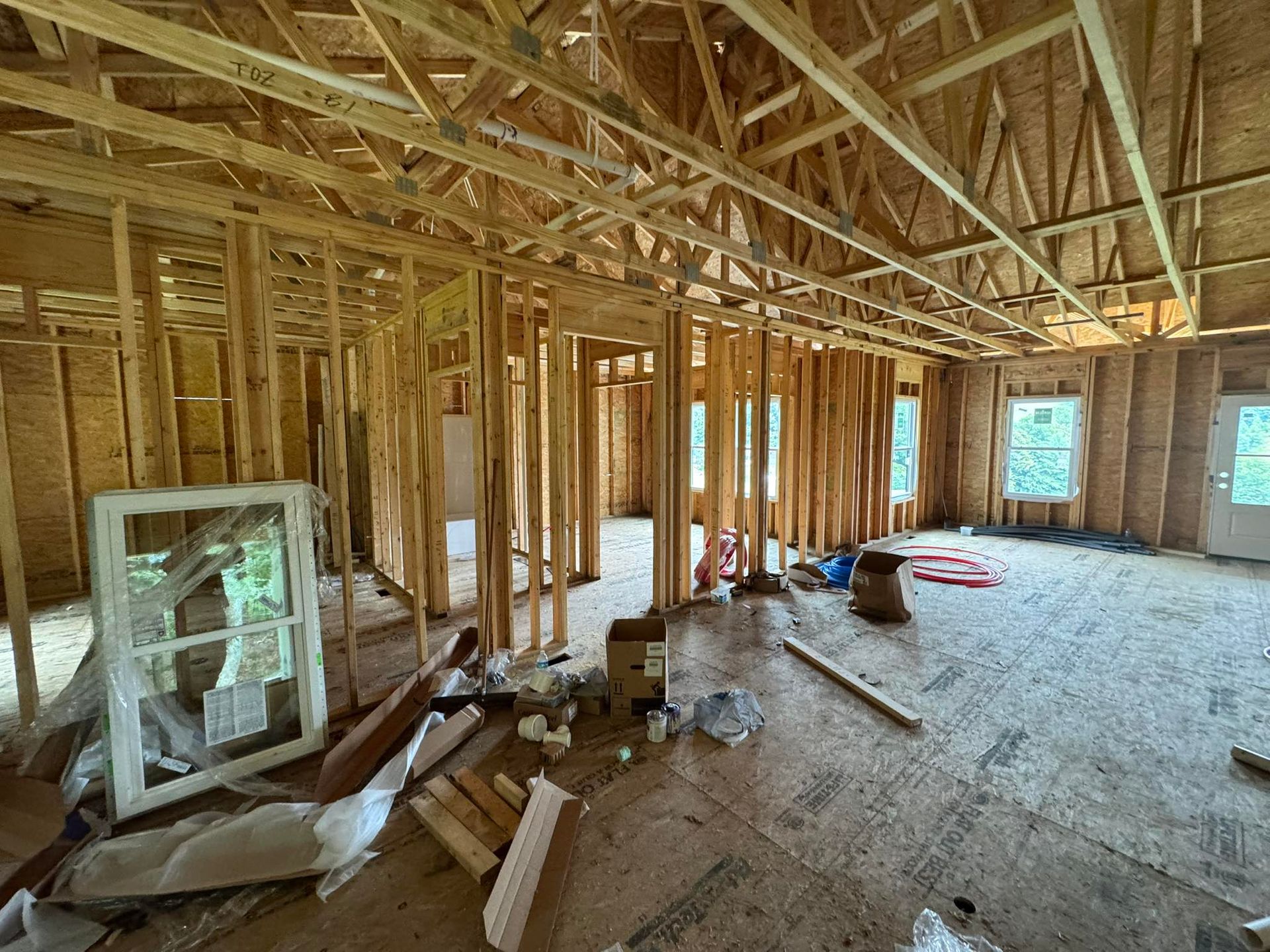 Interior view of a house under construction; wooden frame walls, floor, and ceiling, with debris on the floor.
