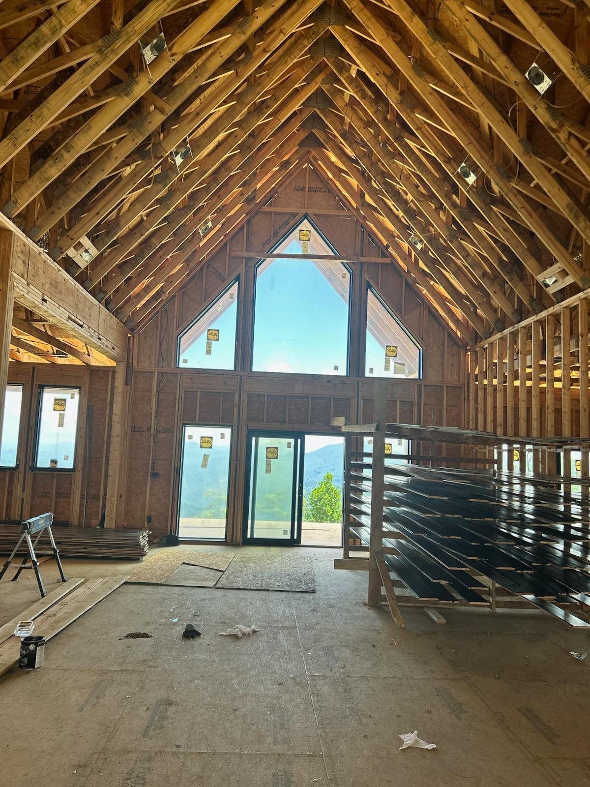Interior of a house under construction; exposed wooden beams and large windows overlooking a mountain view.