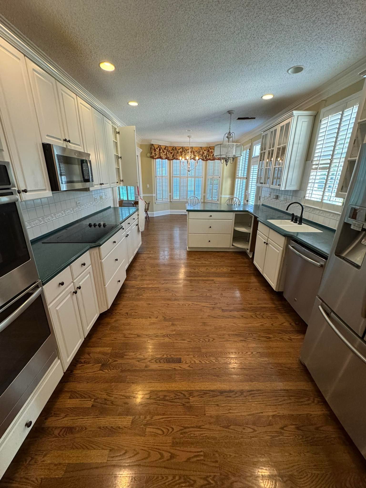 Kitchen with white cabinets, dark countertops, wood floors, stainless steel appliances, and a window.