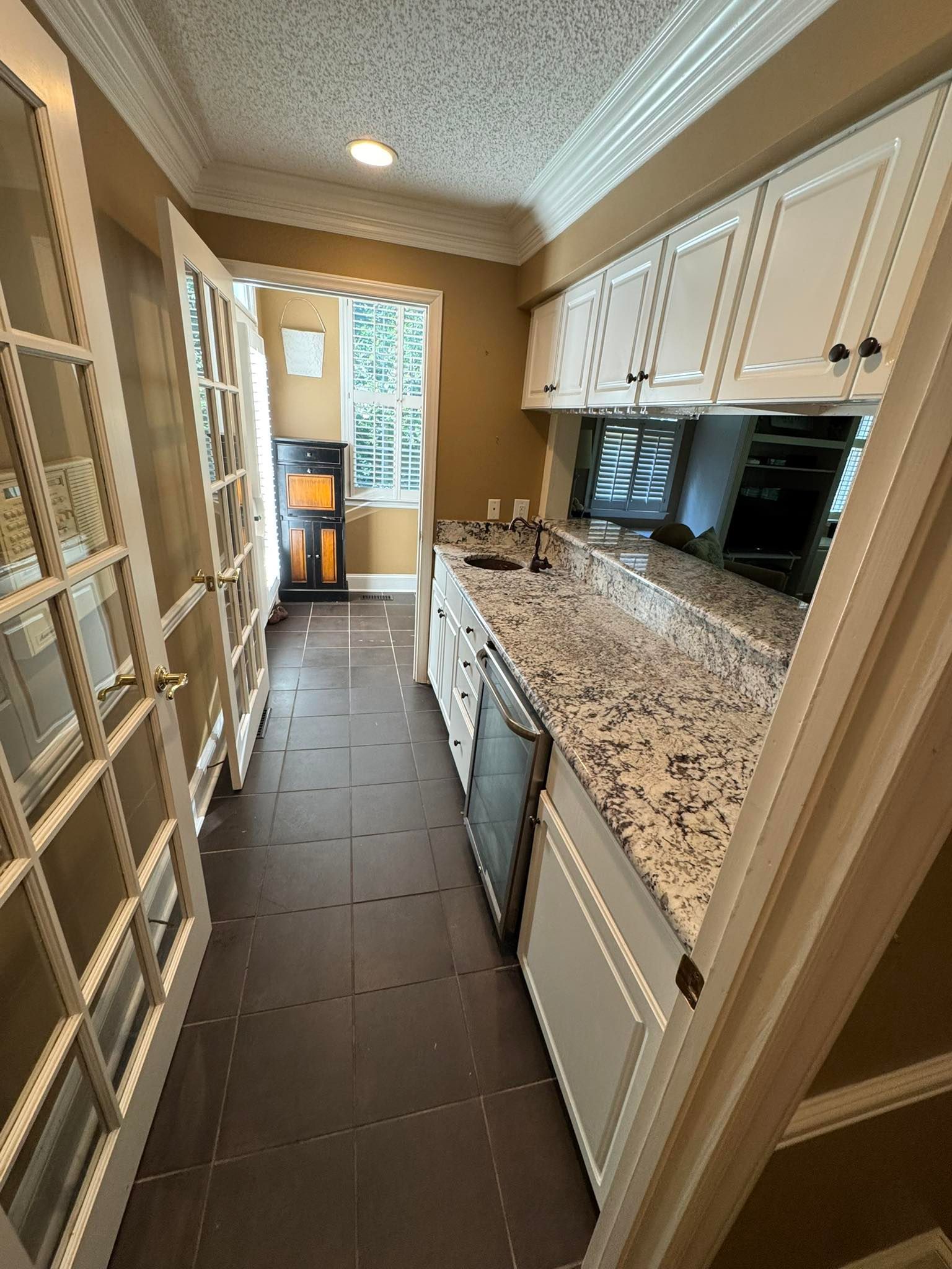 Narrow kitchen with white cabinets, granite countertop, stainless steel appliances, and French doors.