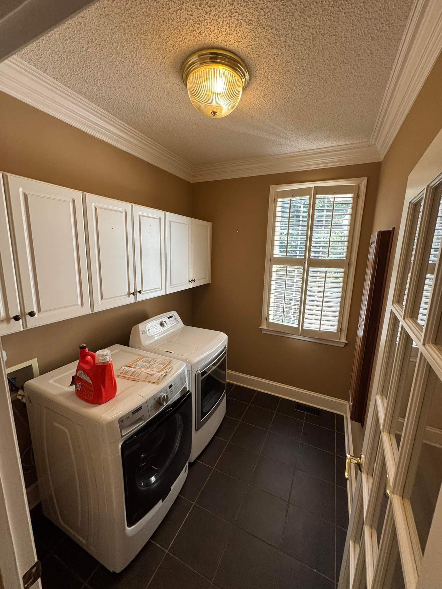 Laundry room with washer, dryer, white cabinets, brown walls, dark floor, and a window.