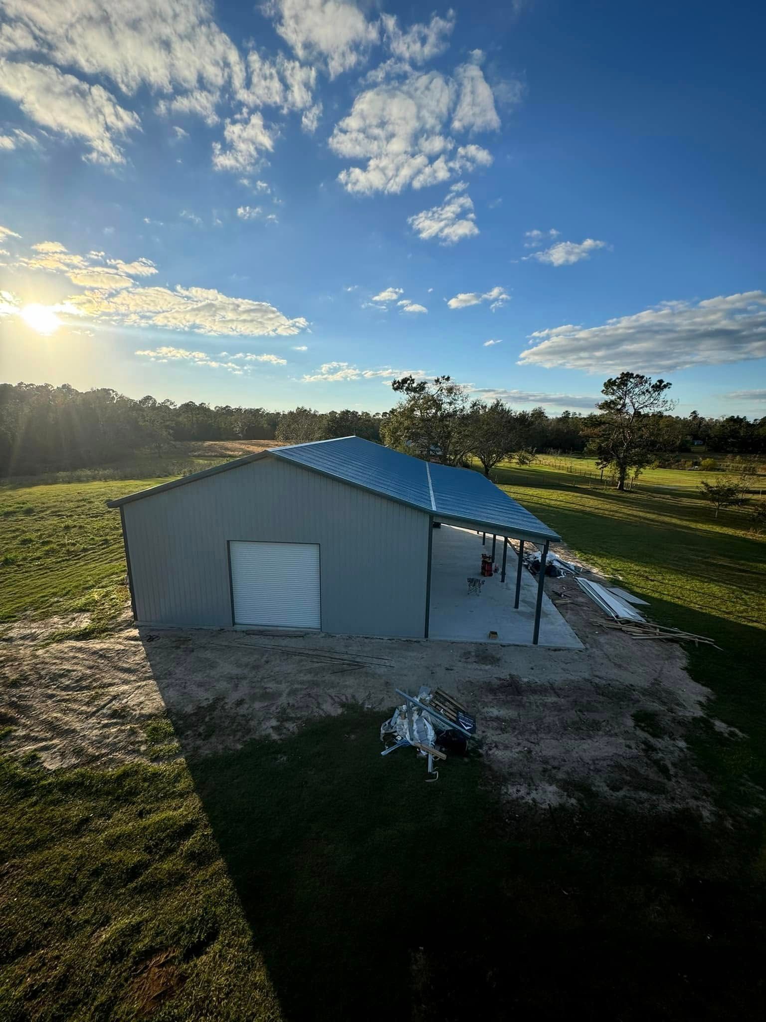 Metal barn with blue roof, open-air awning, and white door. Set in a grassy field under a sunny sky.