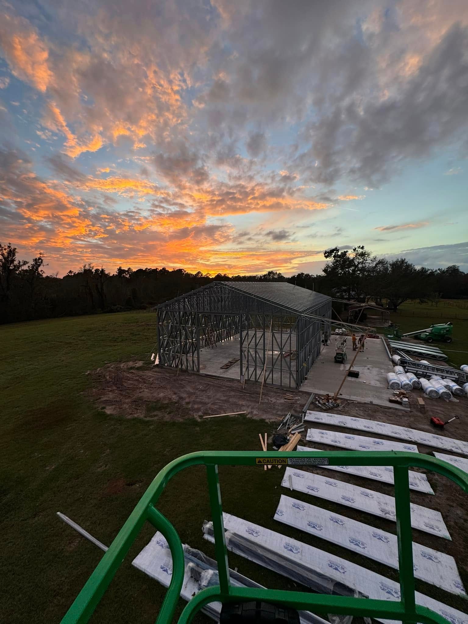 Metal frame of a building under construction at sunset; materials and tools on ground.