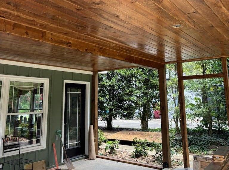 Wood-paneled porch ceiling with overhead lighting. Exterior view of a house, looking onto a yard with trees.