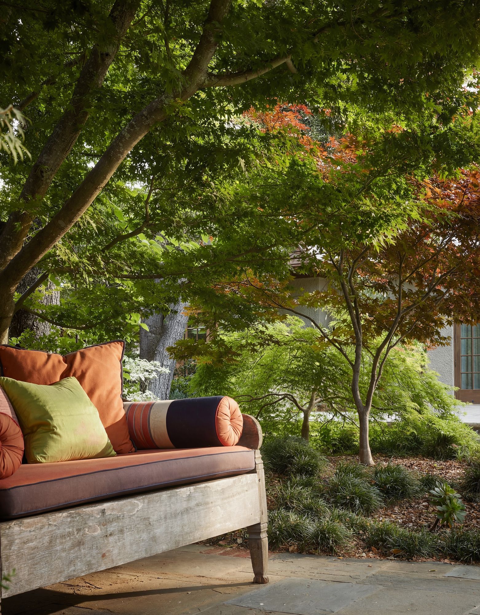 Wooden bench with colorful cushions under trees in a garden.