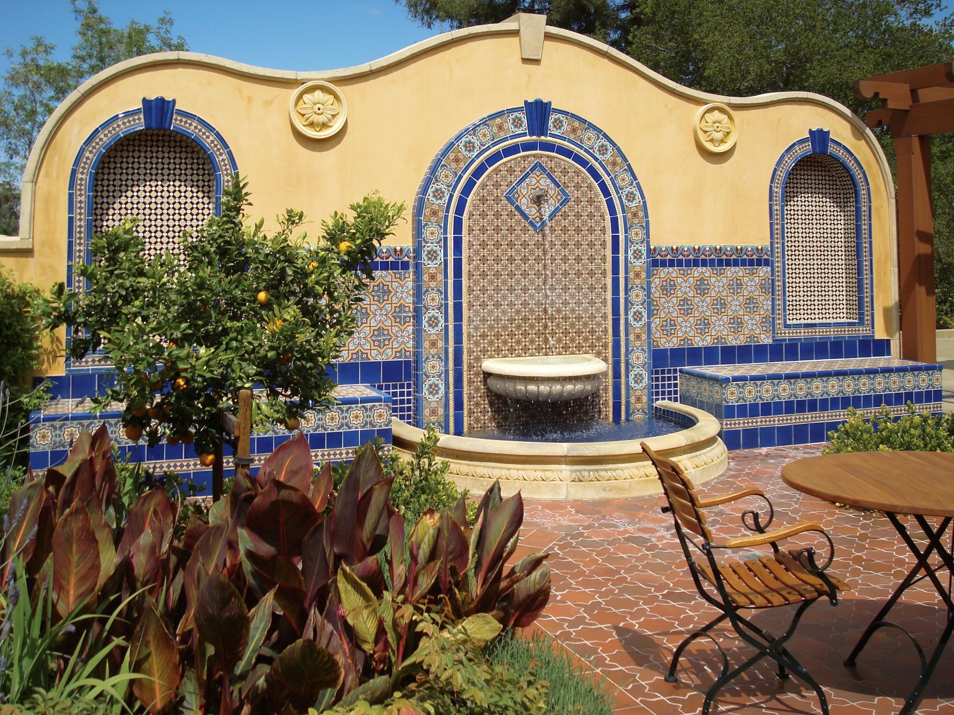 Outdoor water fountain with blue and white tile accents and a yellow stucco wall.