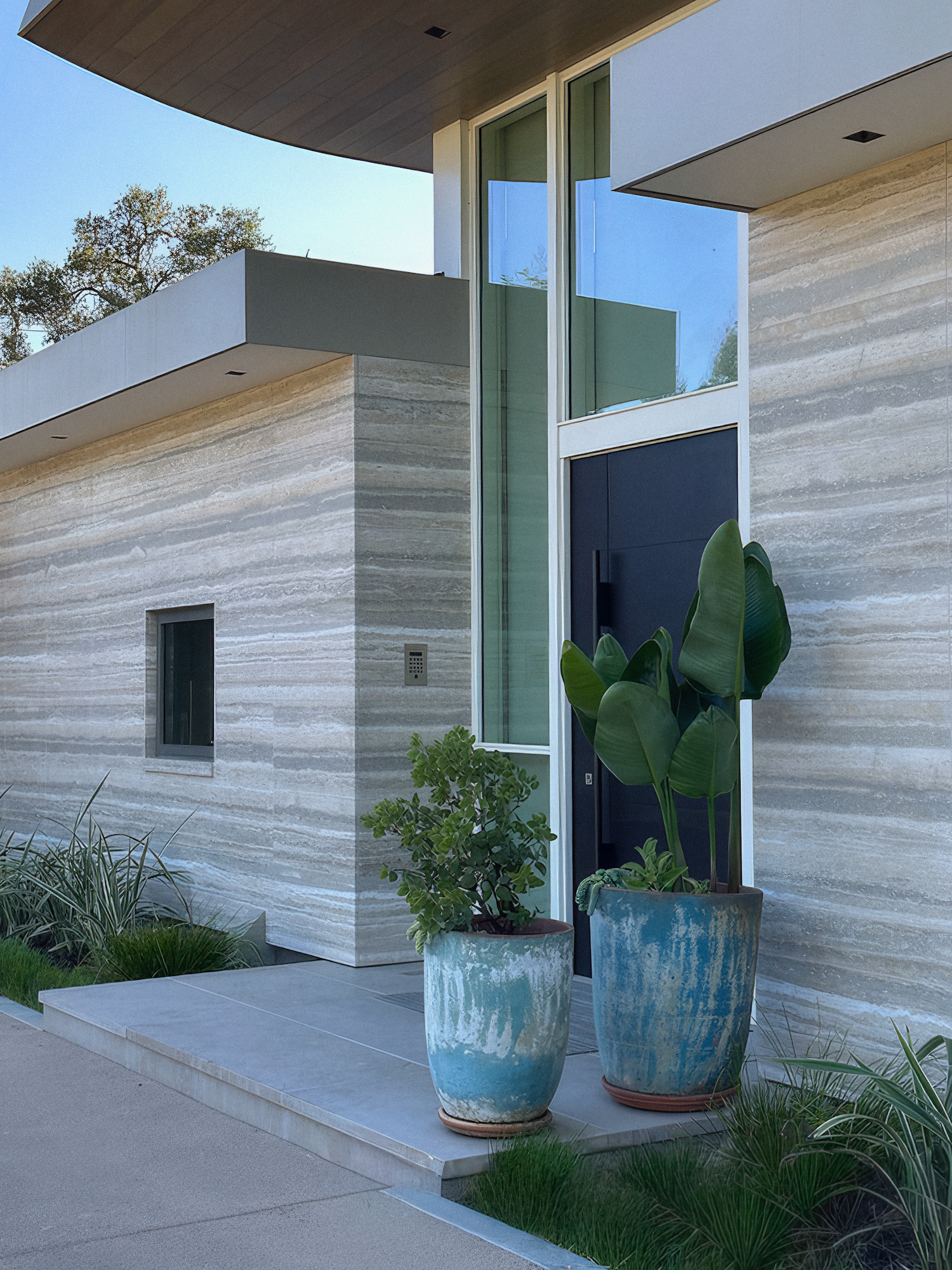 Modern house exterior with stone facade, glass door, and turquoise planters with plants on the porch.