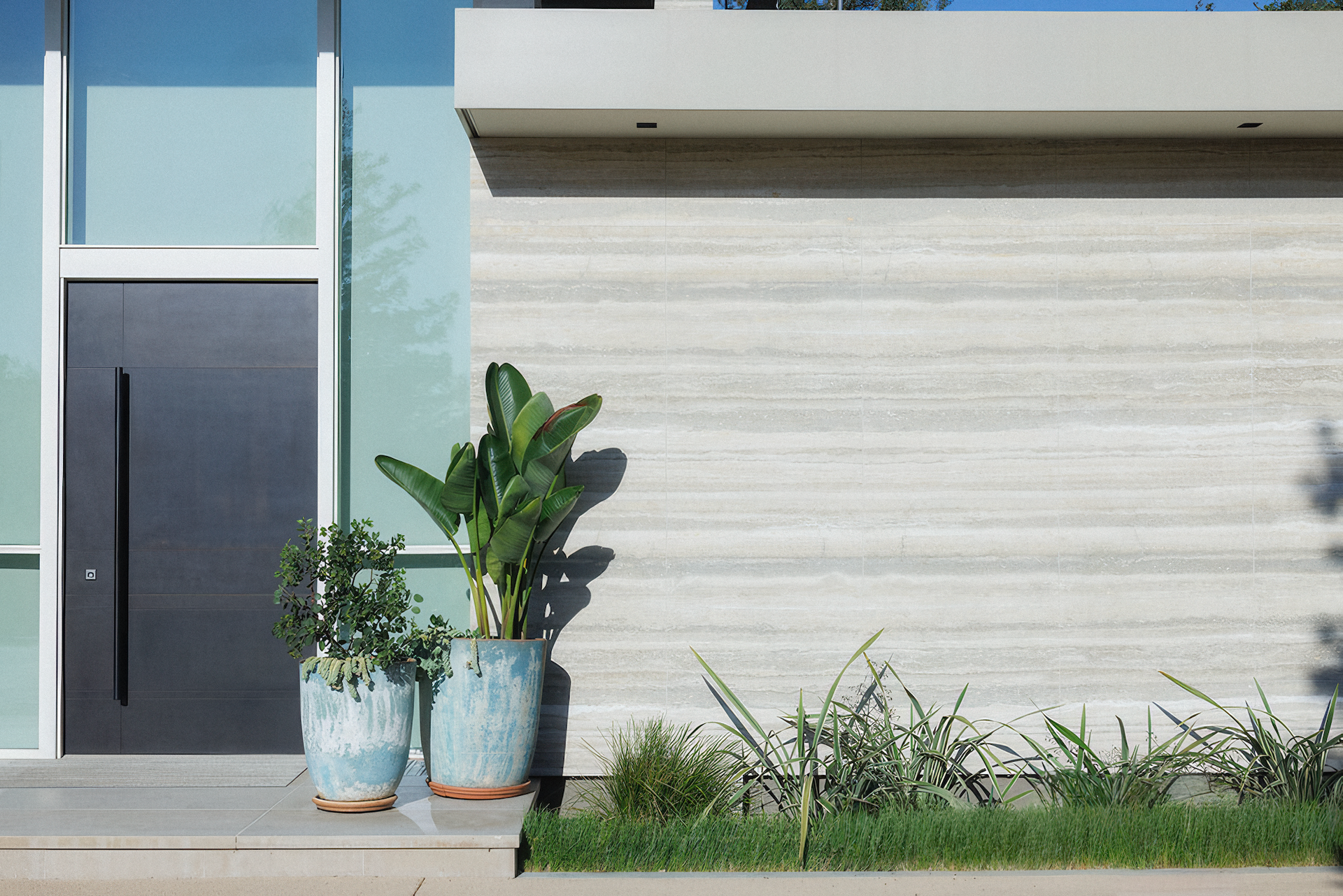 Modern house exterior with gray door, potted plants, and light stone wall.