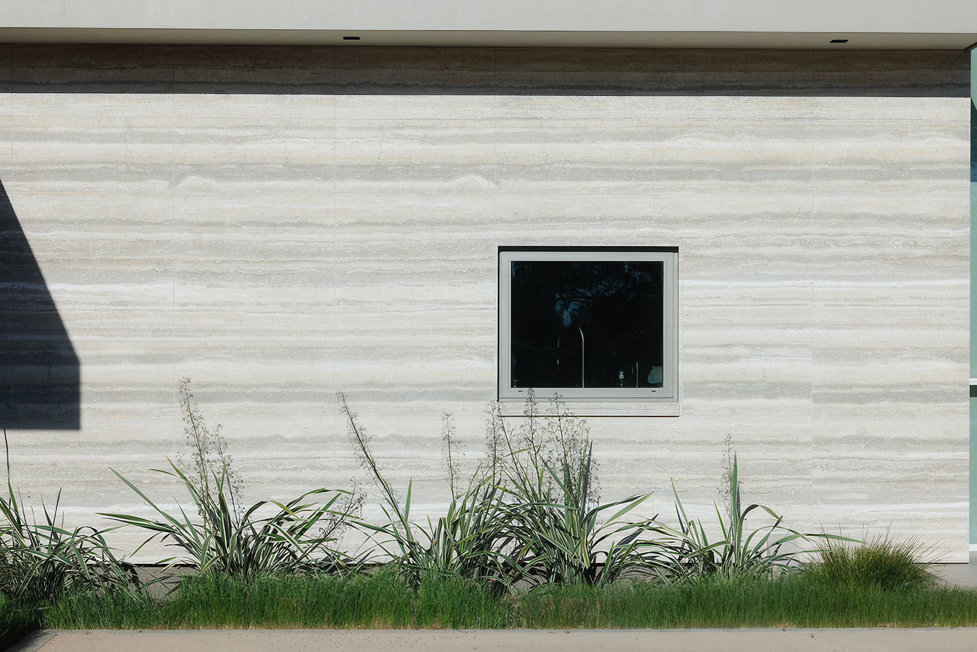 Window on a textured wall with horizontal lines, plants in front.