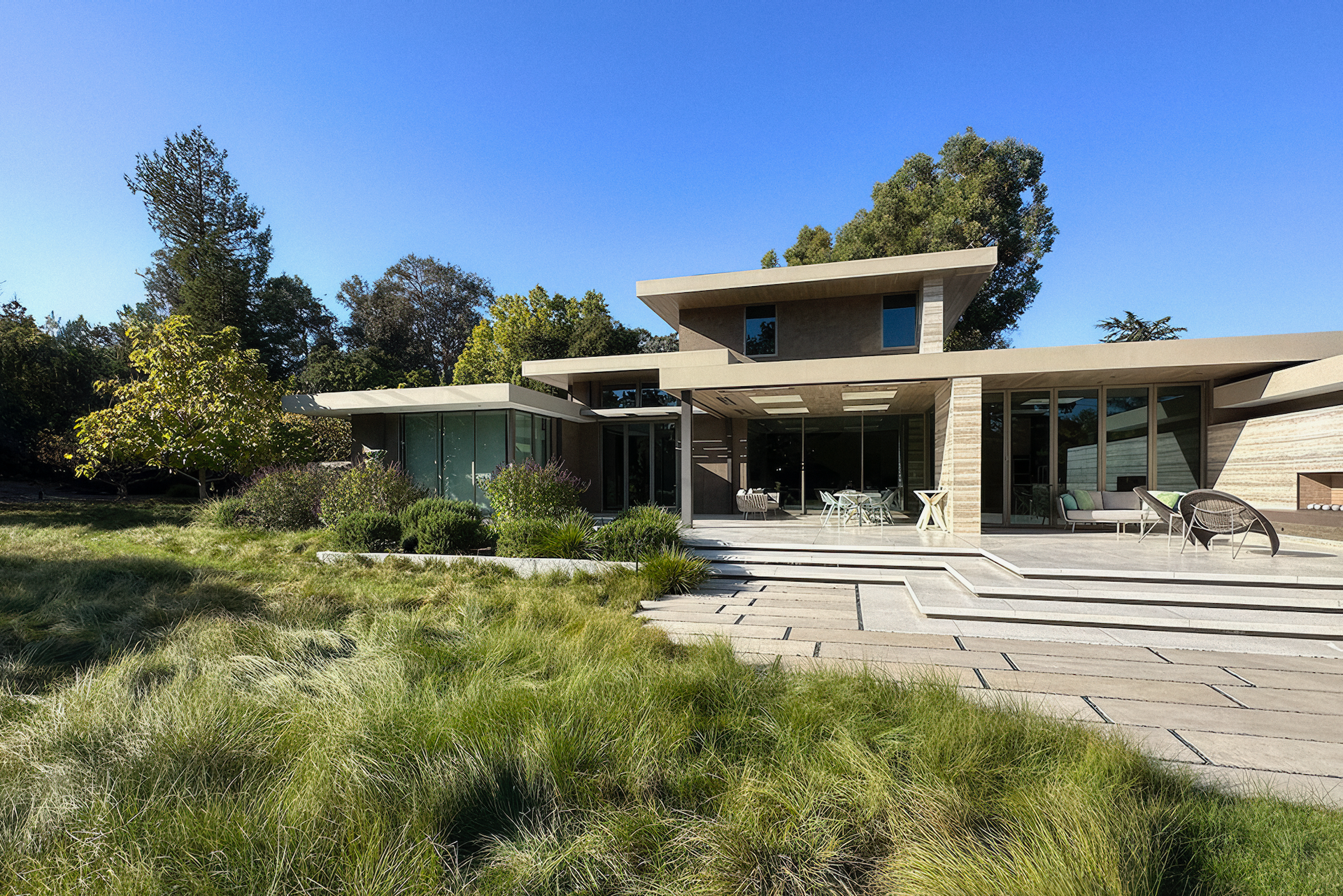 Modern house with large windows and a flat roof, surrounded by green lawn and trees.