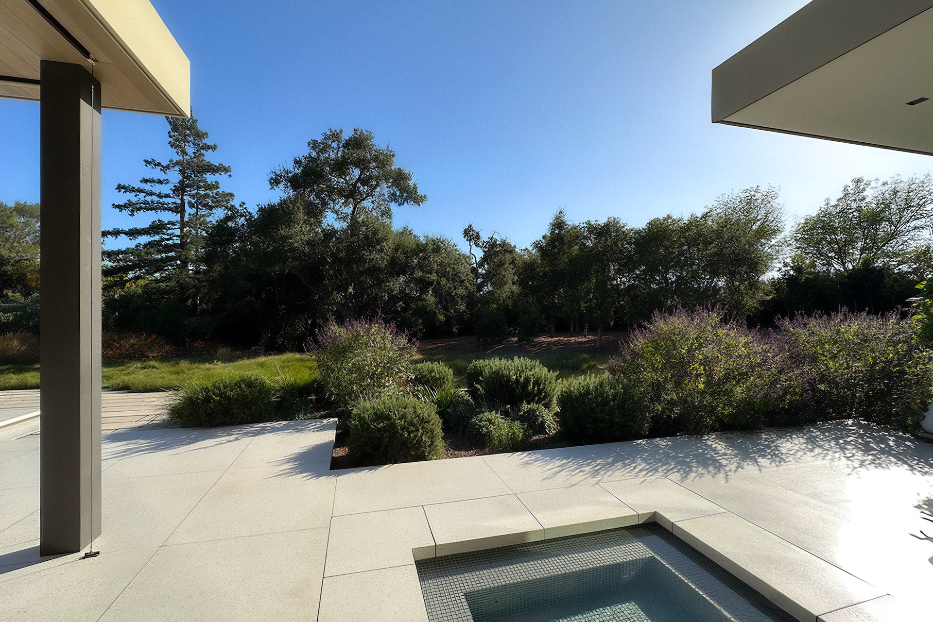 Patio with a pool, looking out over a garden and trees under a clear blue sky.