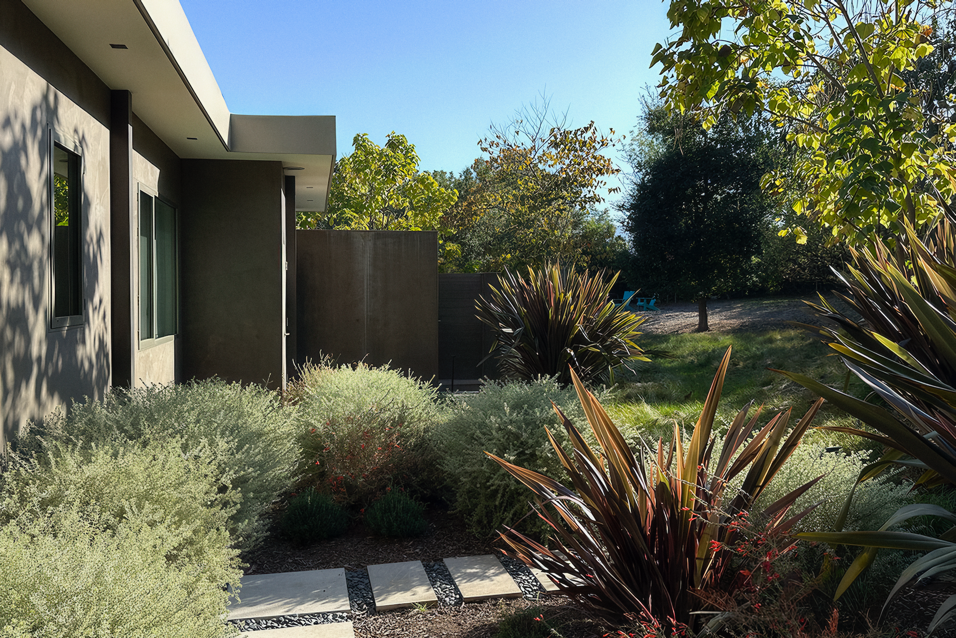 Modern house exterior with lush garden, stone path, and sunny sky.