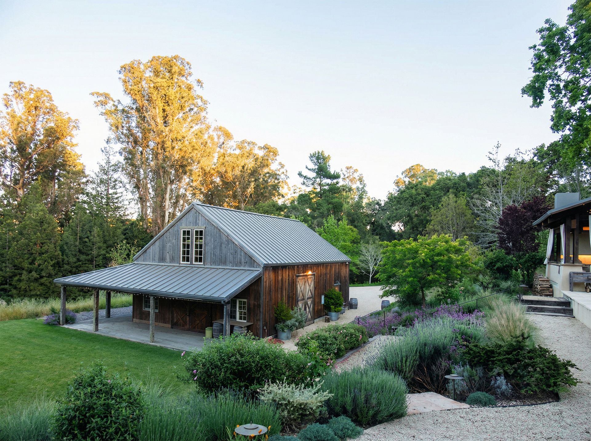 Wooden barn-style building with a covered porch surrounded by a garden and a green lawn.