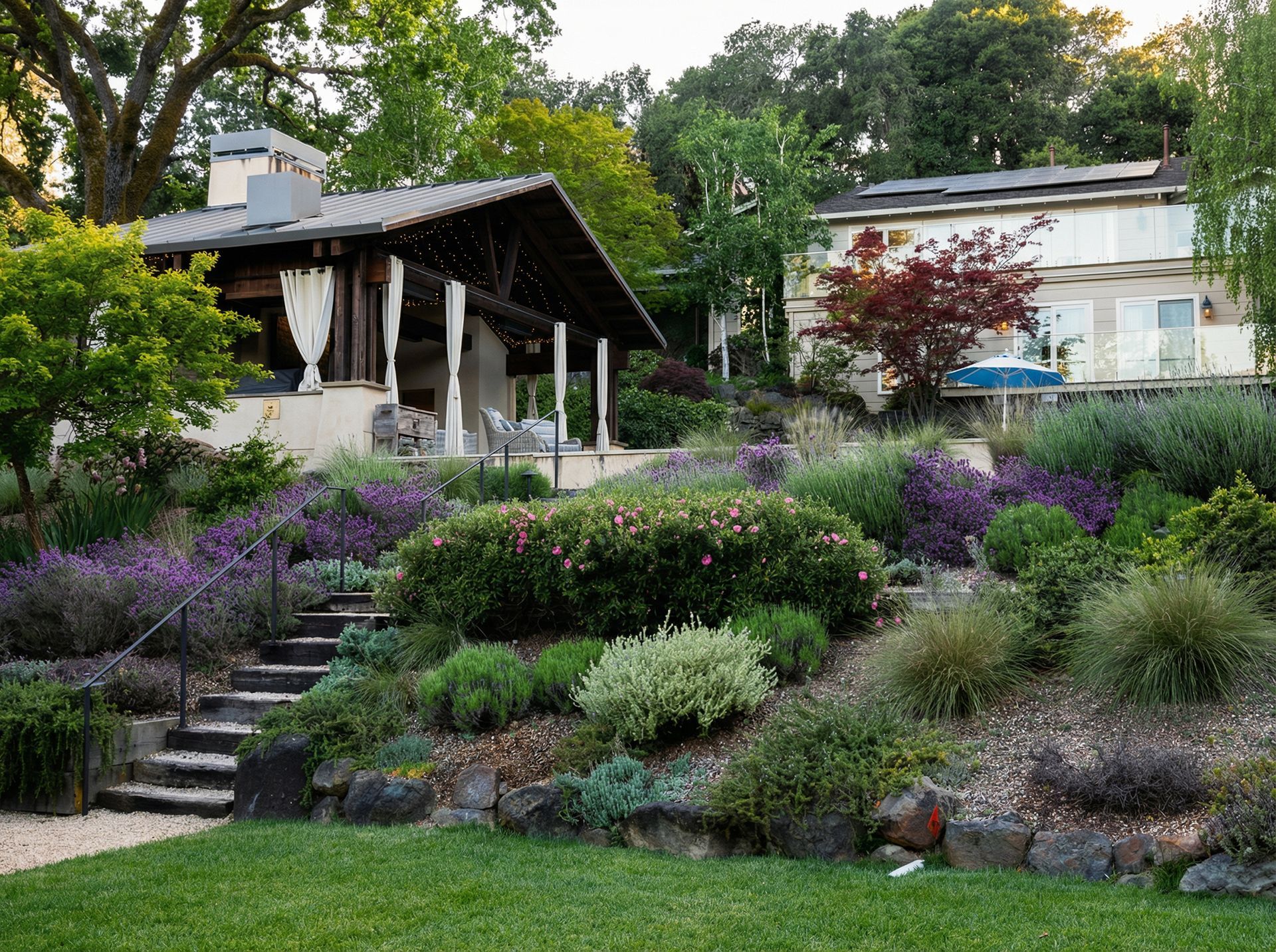 A terraced garden with lavender and shrubs leads up to a covered patio and a two-story building.