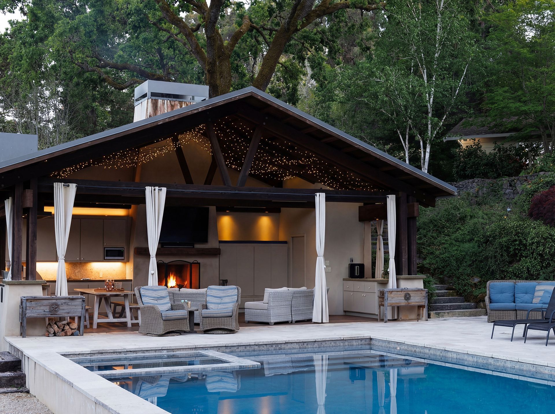 Outdoor pool with a covered kitchen and seating area, lit with string lights.