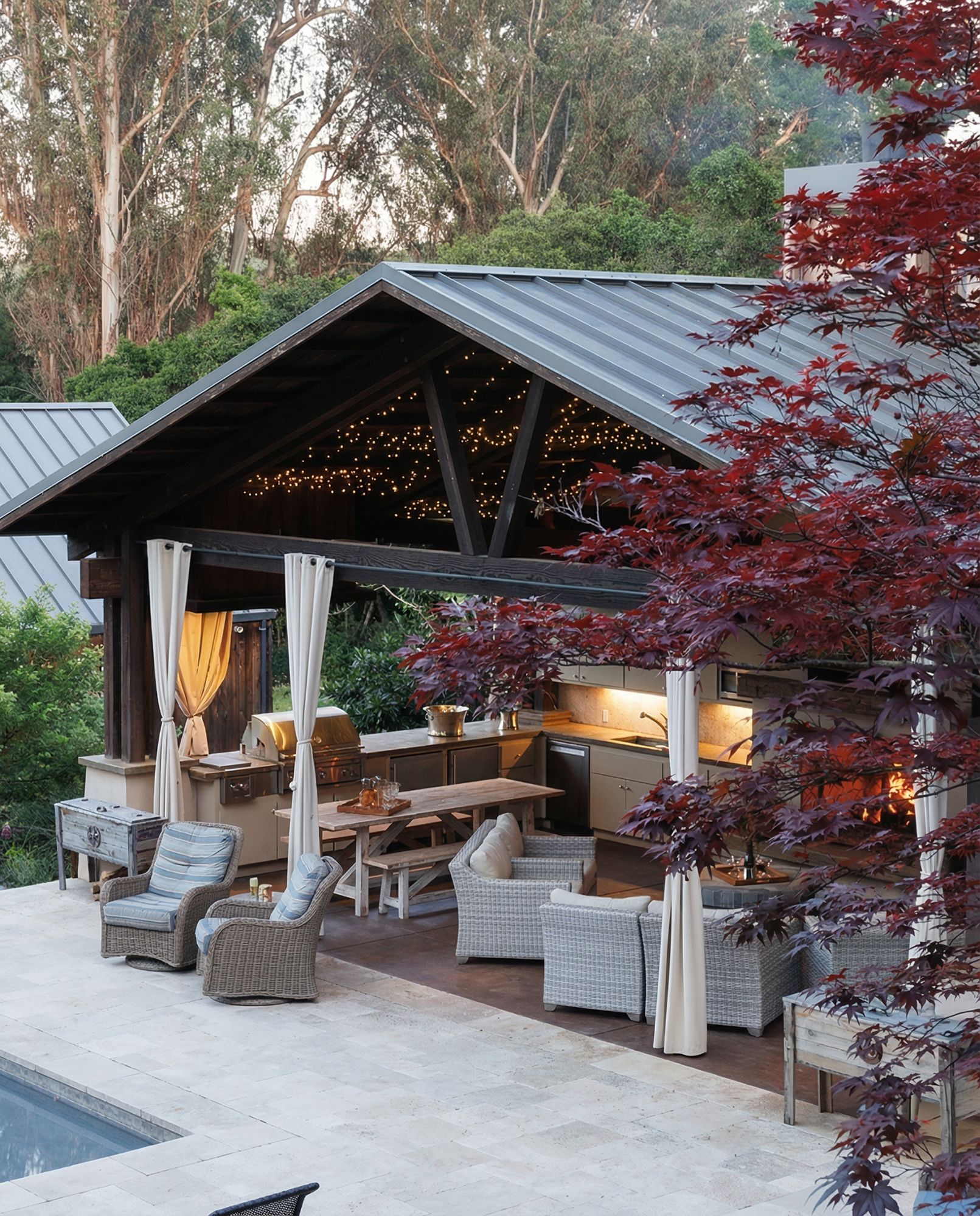 Outdoor kitchen and dining area with a metal roof, seating, and a large Japanese maple.