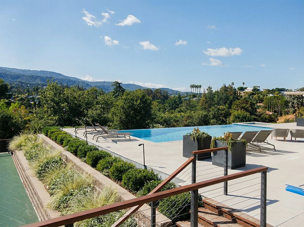 An infinity pool overlooking a green landscape and mountains on a sunny day.