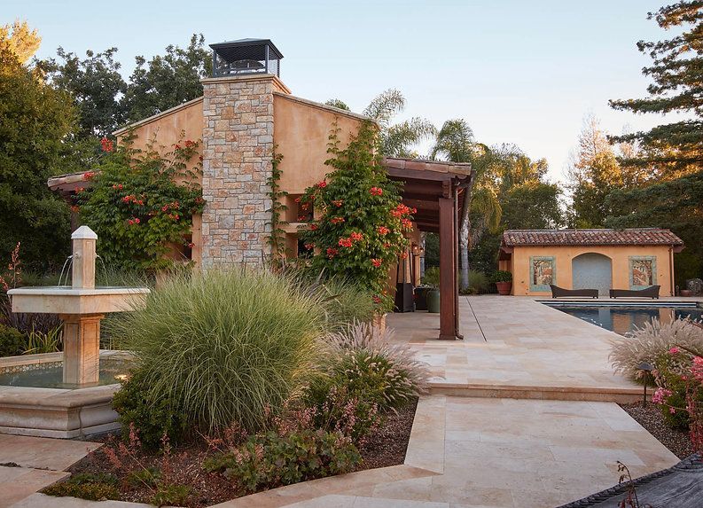 Beige stucco house with fountain, pool, pergola, and lush landscaping.